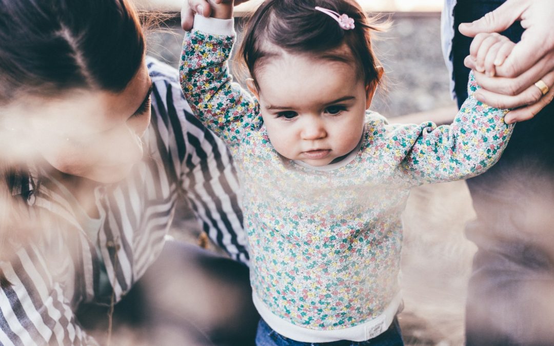 woman holding girl while learning to walk taken at daytime