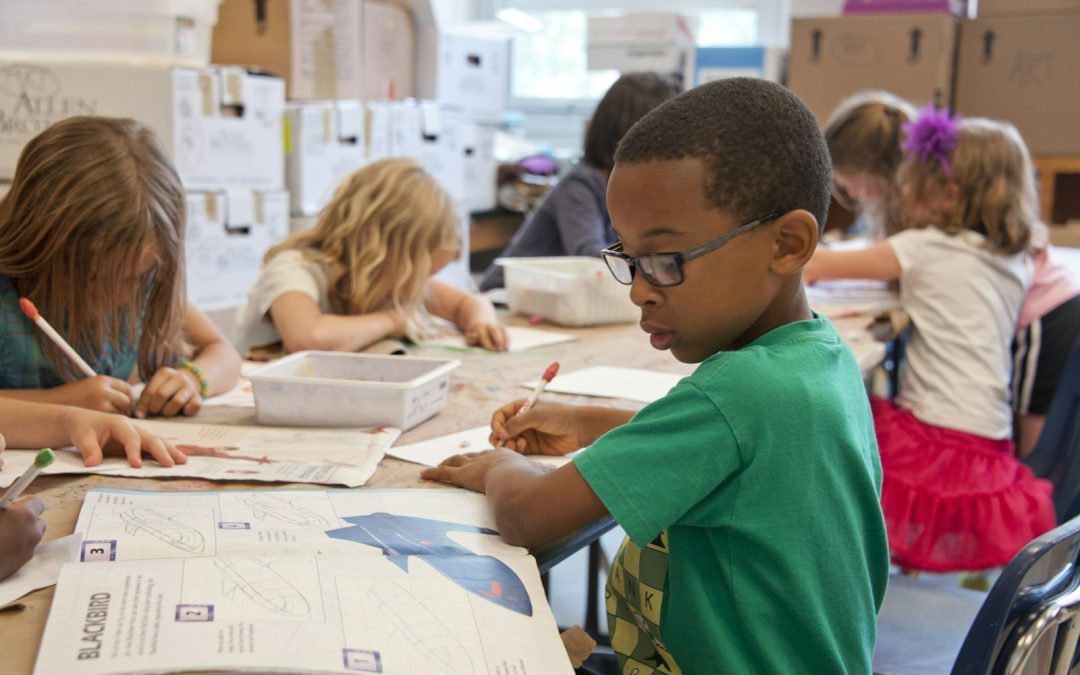 boy in green sweater writing on white paper