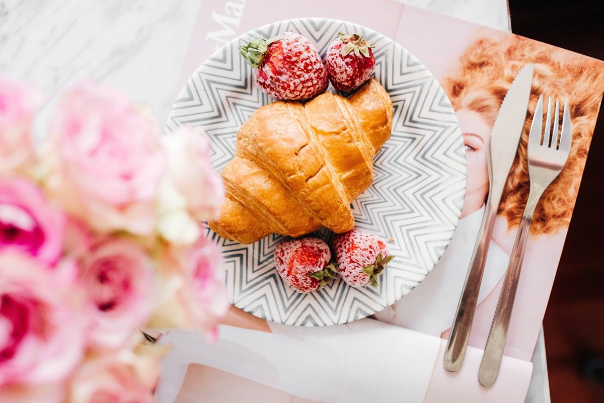 croissant bread and stawberries on beside fork and knife